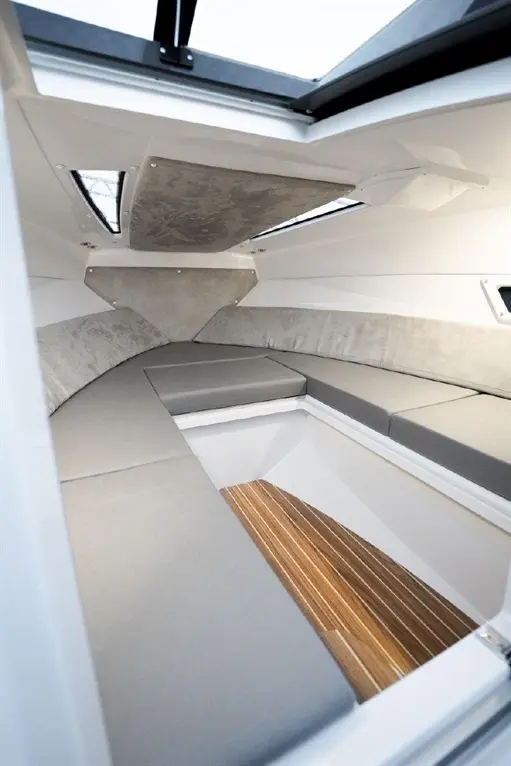 Interior of a modern boat featuring grey upholstery, a wooden floor, and overhead windows for natural light.